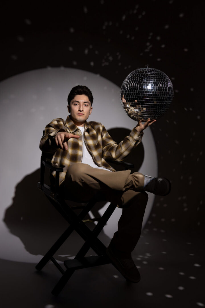 Man seated holding disco ball pointing forward