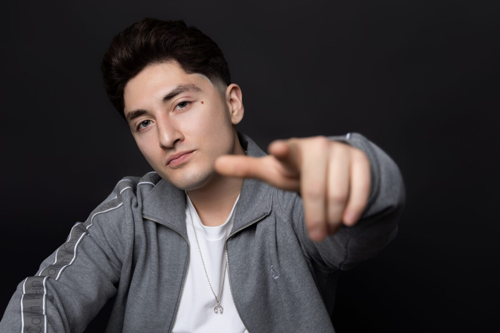 Young man in gray jacket pointing at camera